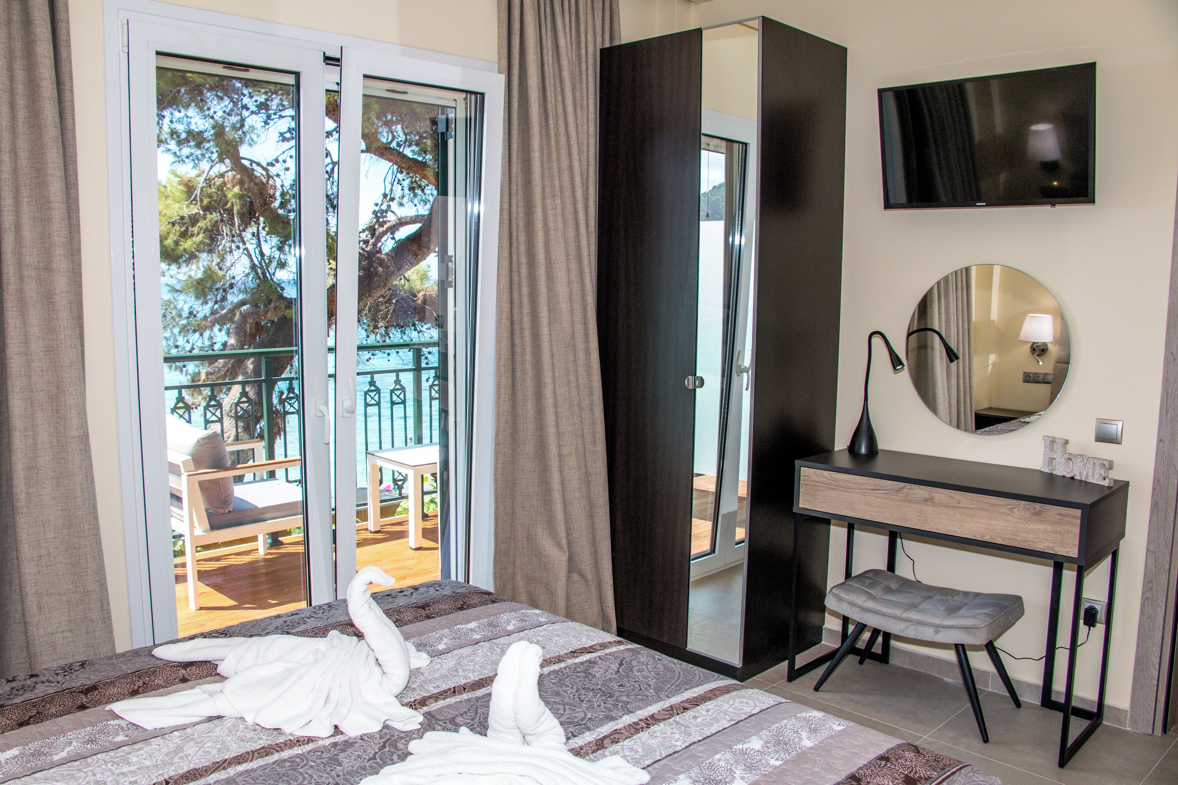 A hotel room with a bed, a desk, a chair, a TV, and a large window with a view of the outdoors.