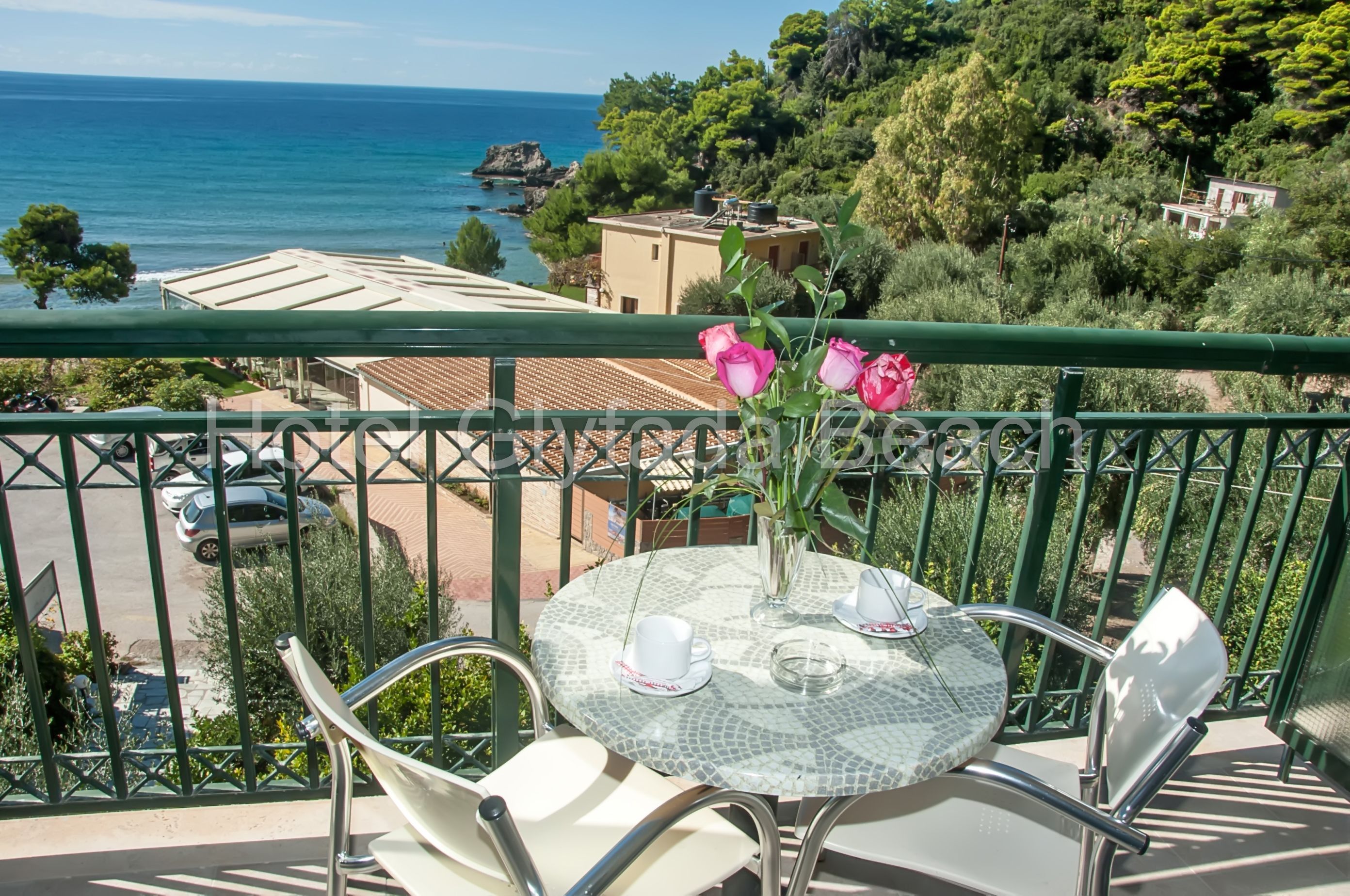 Un balcon avec une table et des chaises, donnant sur une zone côtière bordée d’arbres et de bâtiments.