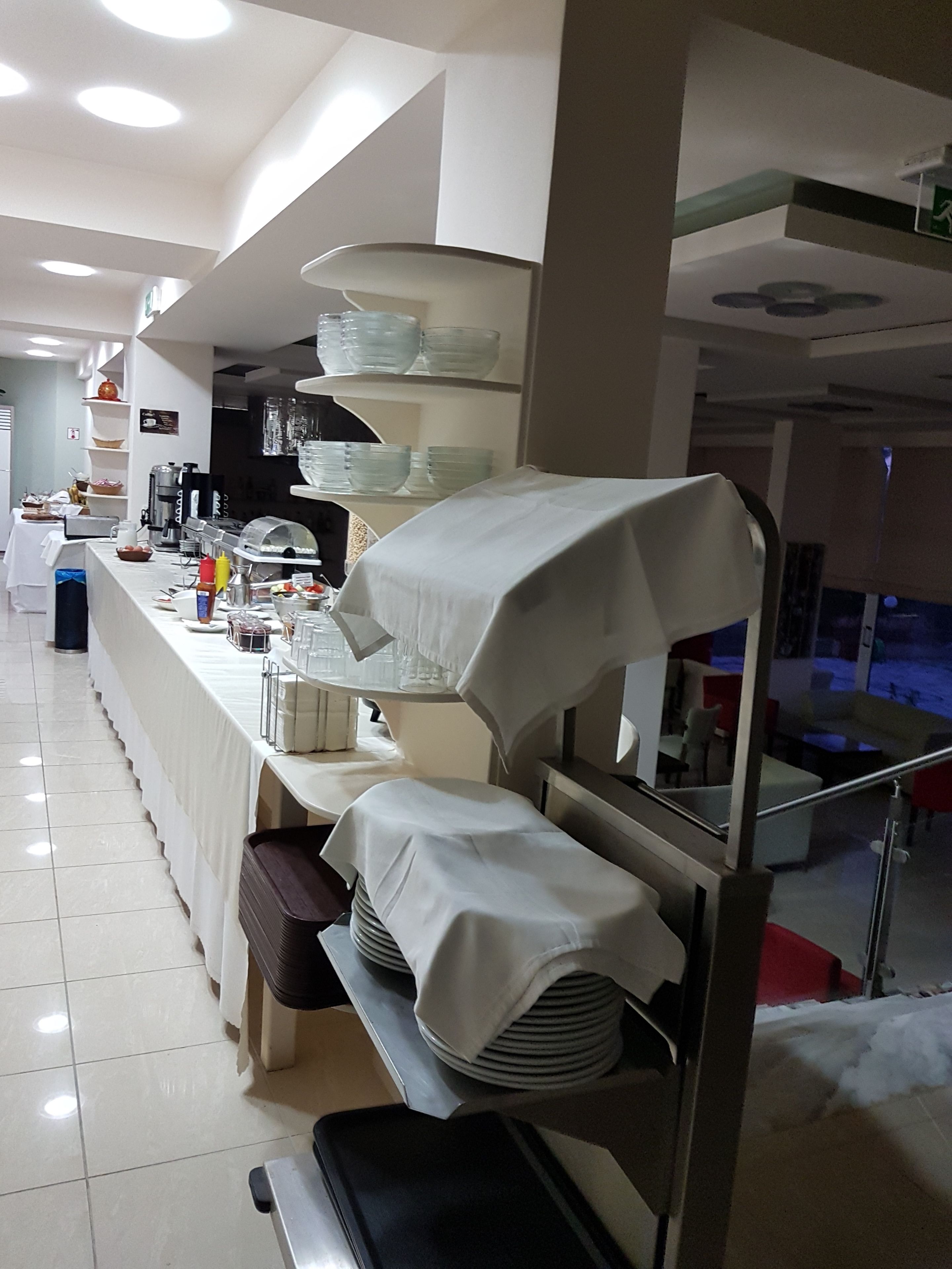 A buffet setup with a long counter, covered food display, and stacked plates.
