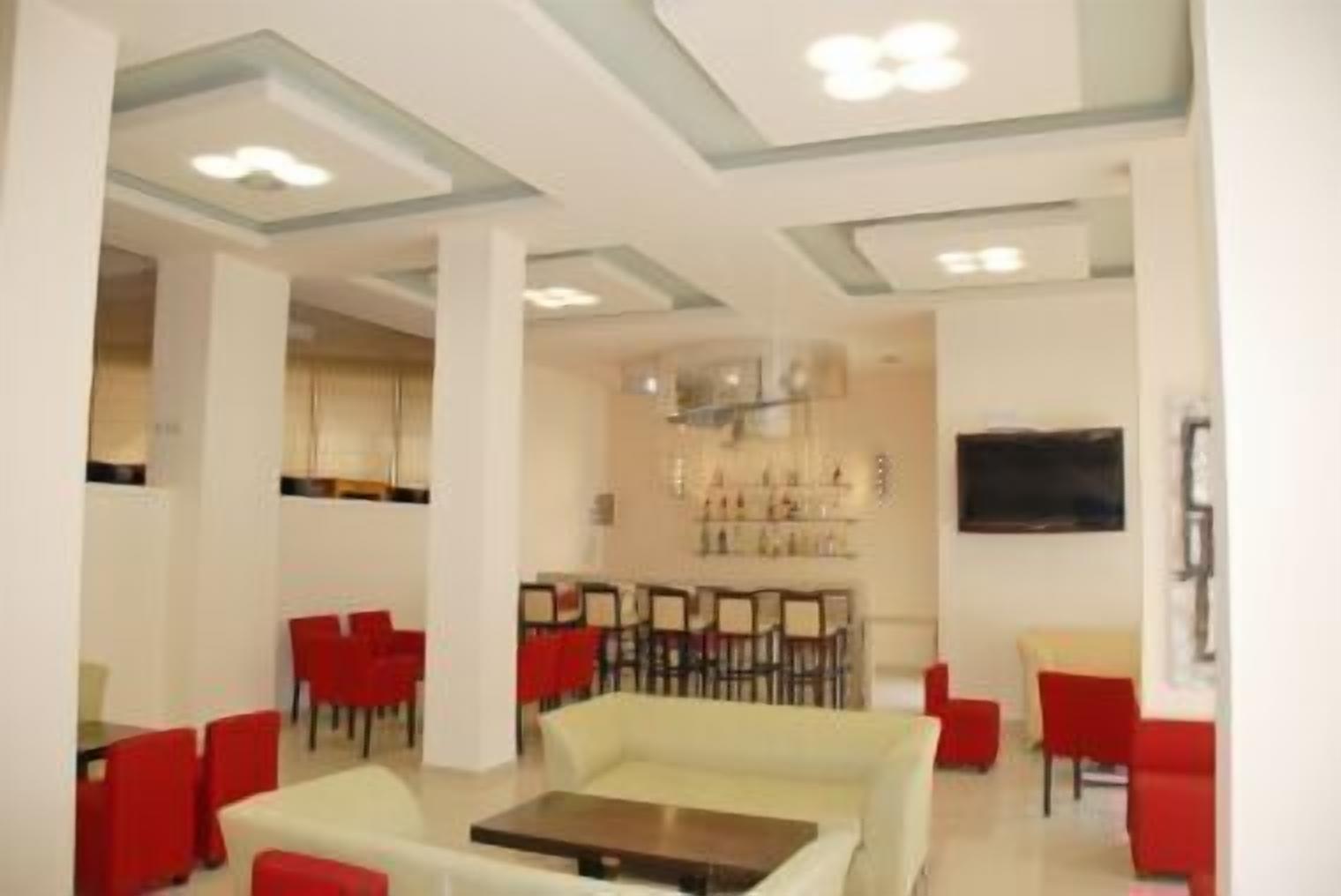 A modern hotel lobby with a central seating area, a bar, and a television mounted on the wall.