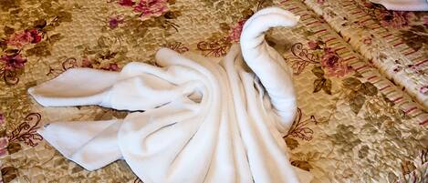 A bed with a floral patterned bedspread and a white towel folded in a swan shape.