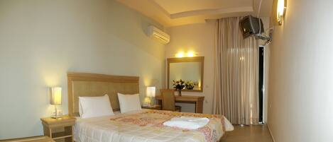 A hotel room with a bed, bedside lamps, a desk with a mirror, and a TV mounted on the wall.