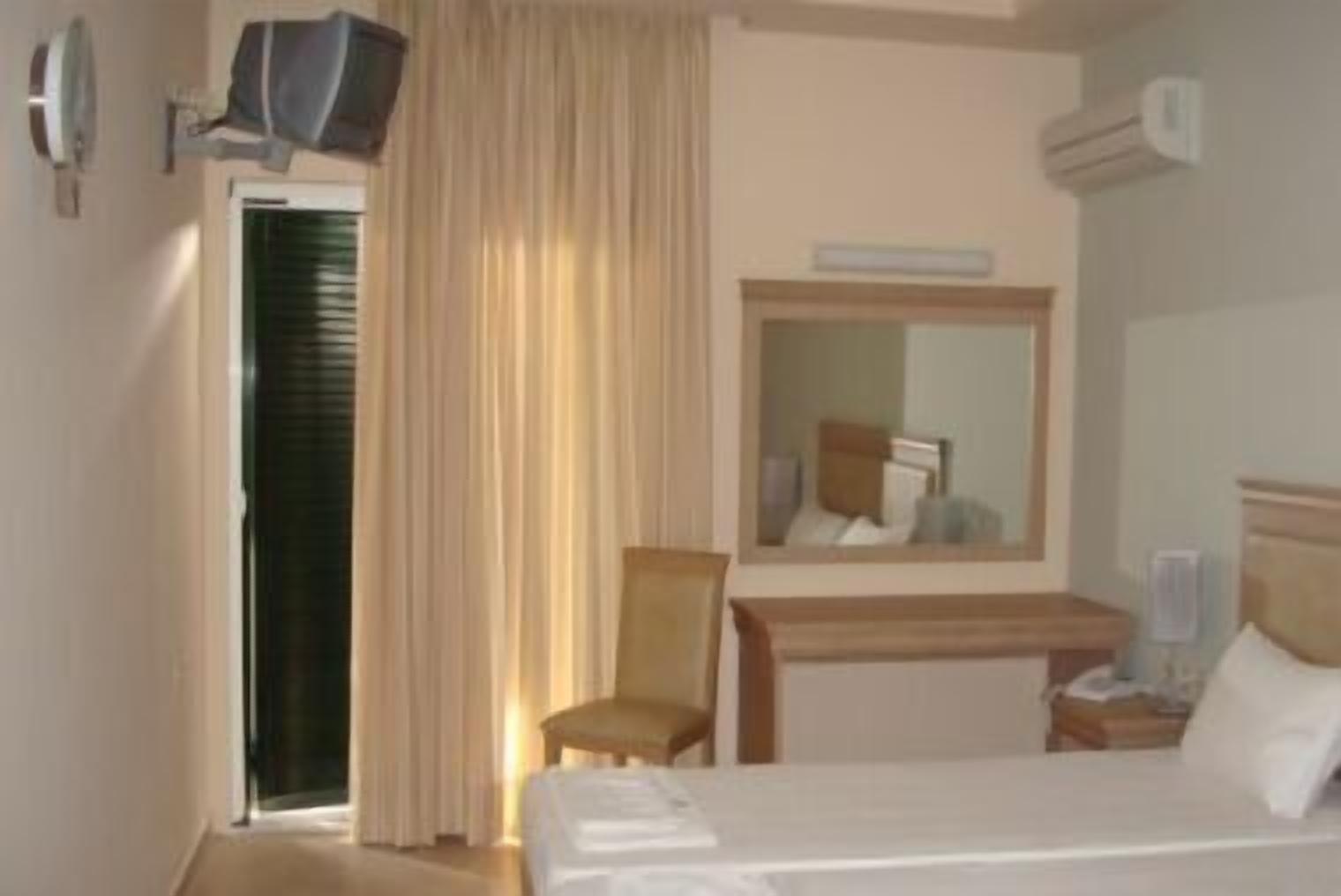 A hotel room with a bed, a desk with a chair, a television, and a mirror.