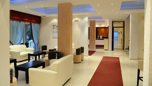 A modern hotel lobby with a reception desk, seating area, and a view of the reception. - Primavera Hotel (Corfu)