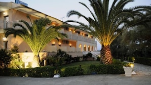 A hotel with a multi-story structure, balconies, and a well-maintained garden with palm trees. - Primavera Hotel (Corfu)