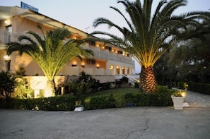 A hotel with a multi-story structure, balconies, and a well-maintained garden with palm trees. - Primavera Hotel (Corfu)