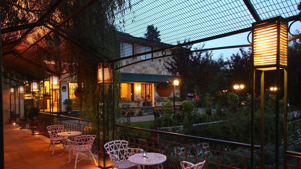 An outdoor patio area with white metal chairs and tables, a covered seating area, and a view of a building with a stone facade.