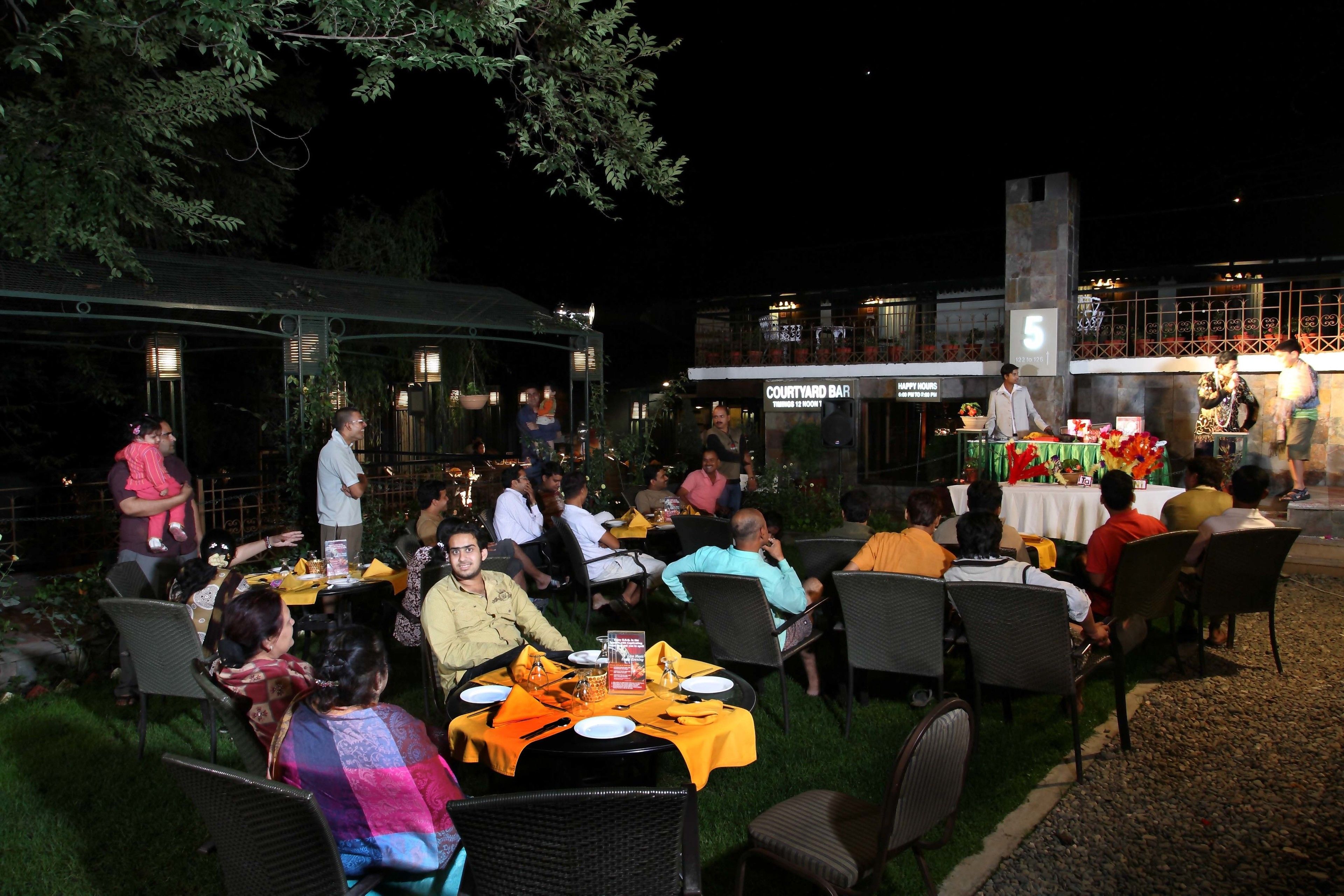 An outdoor dining area with tables and chairs, surrounded by greenery and a building with a sign reading "Courtyard Bar".