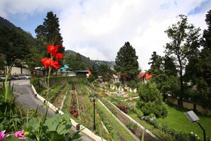 Un jardín con diversas plantas y flores, un sendero y un edificio con techo rojo al fondo.