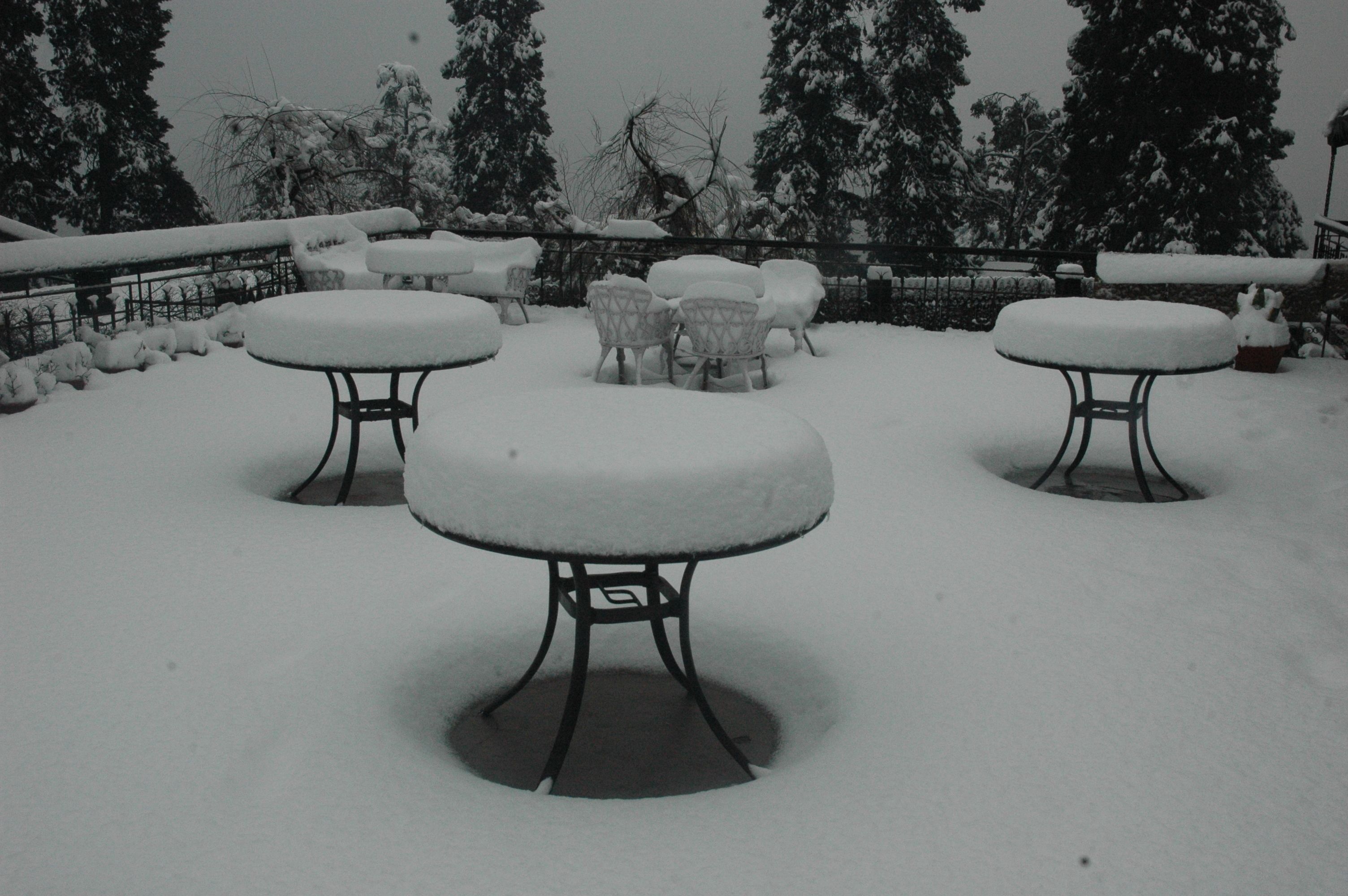A snow-covered outdoor seating area with round tables and chairs.