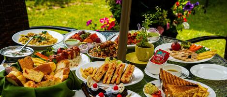 Una mesa al aire libre con diversos platos, como sándwiches, papas fritas y un postre.