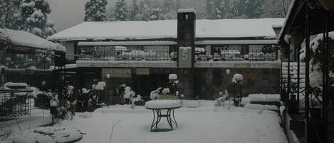 A courtyard with a snow-covered table and chairs, a sign for a courtyard bar, and a building with a snow-covered roof.
