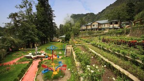 A hotel with a garden, playground, and a view of a mountainous area.