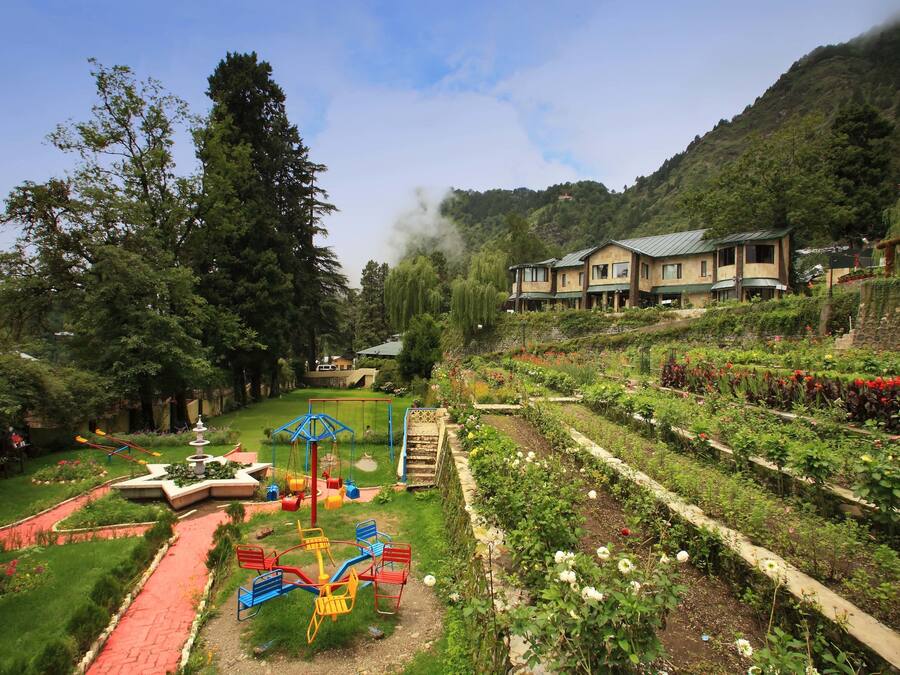 A hotel with a garden, playground, and a view of a mountainous area.