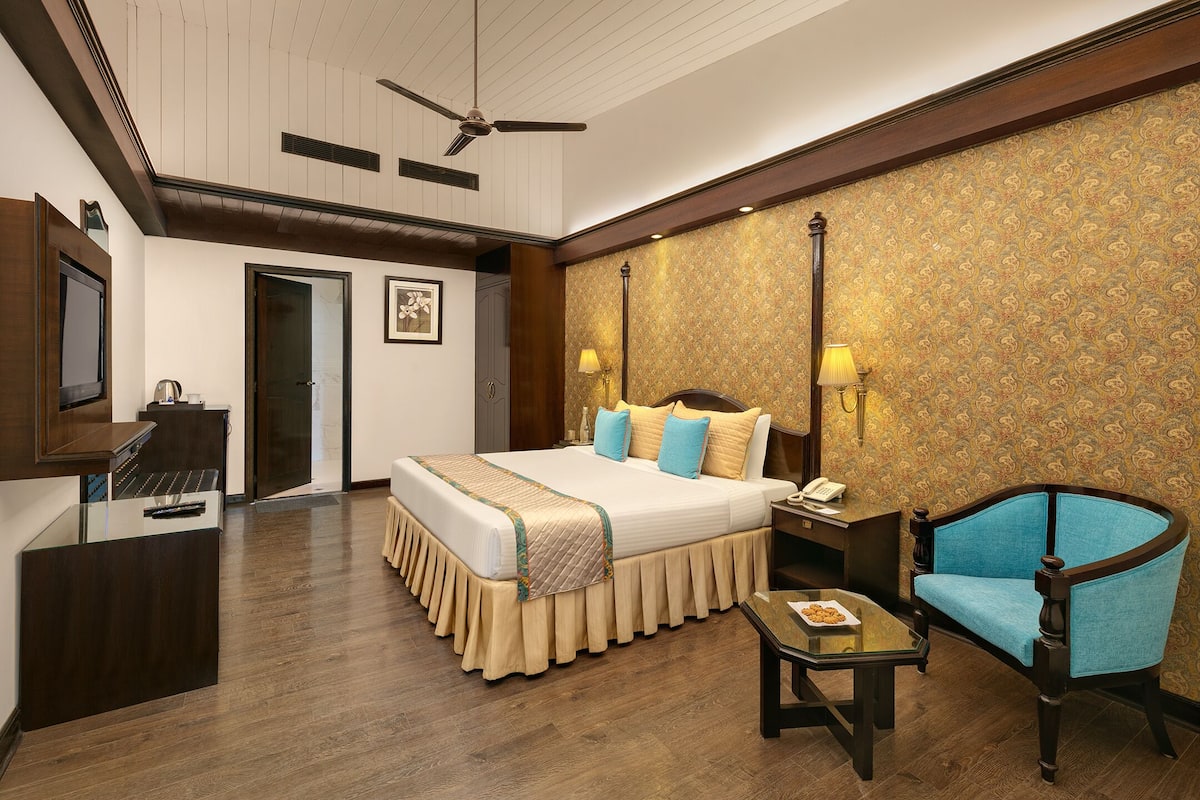 A hotel room with a large bed, a desk, a chair, a ceiling fan, and a patterned wallpaper.