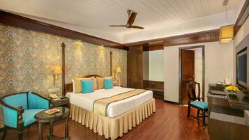 A hotel room with a large bed, a desk, a chair, a small table, and a ceiling fan.