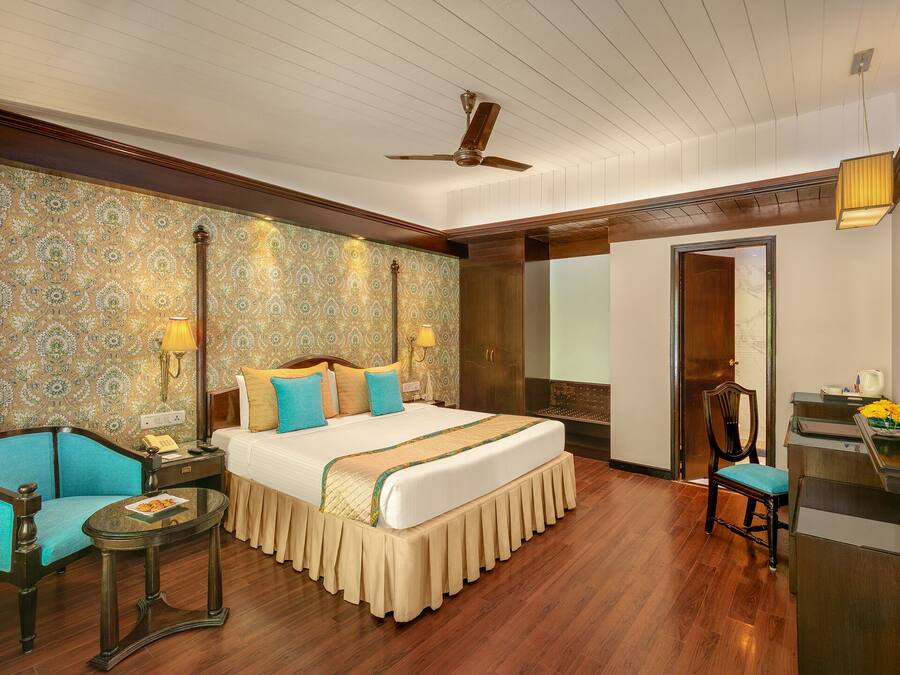A hotel room with a large bed, a desk, a chair, a small table, and a ceiling fan.