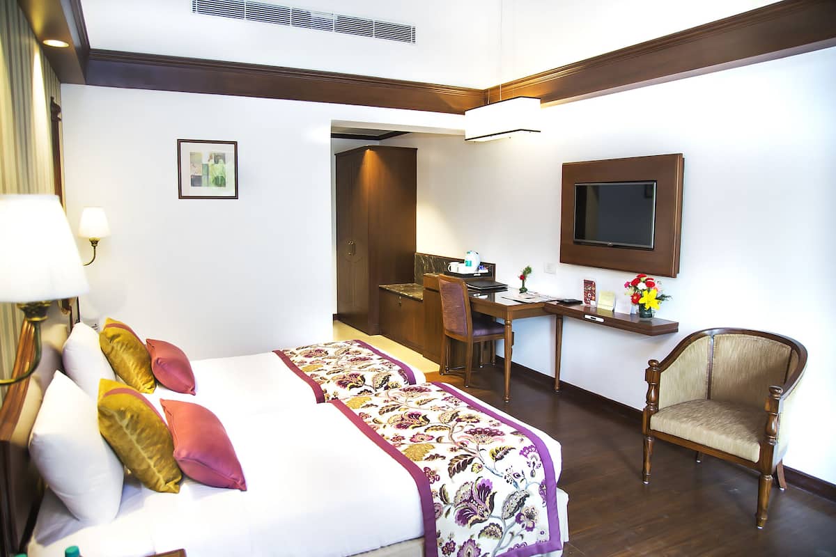 A hotel room with a bed, a desk, a chair, and a television.