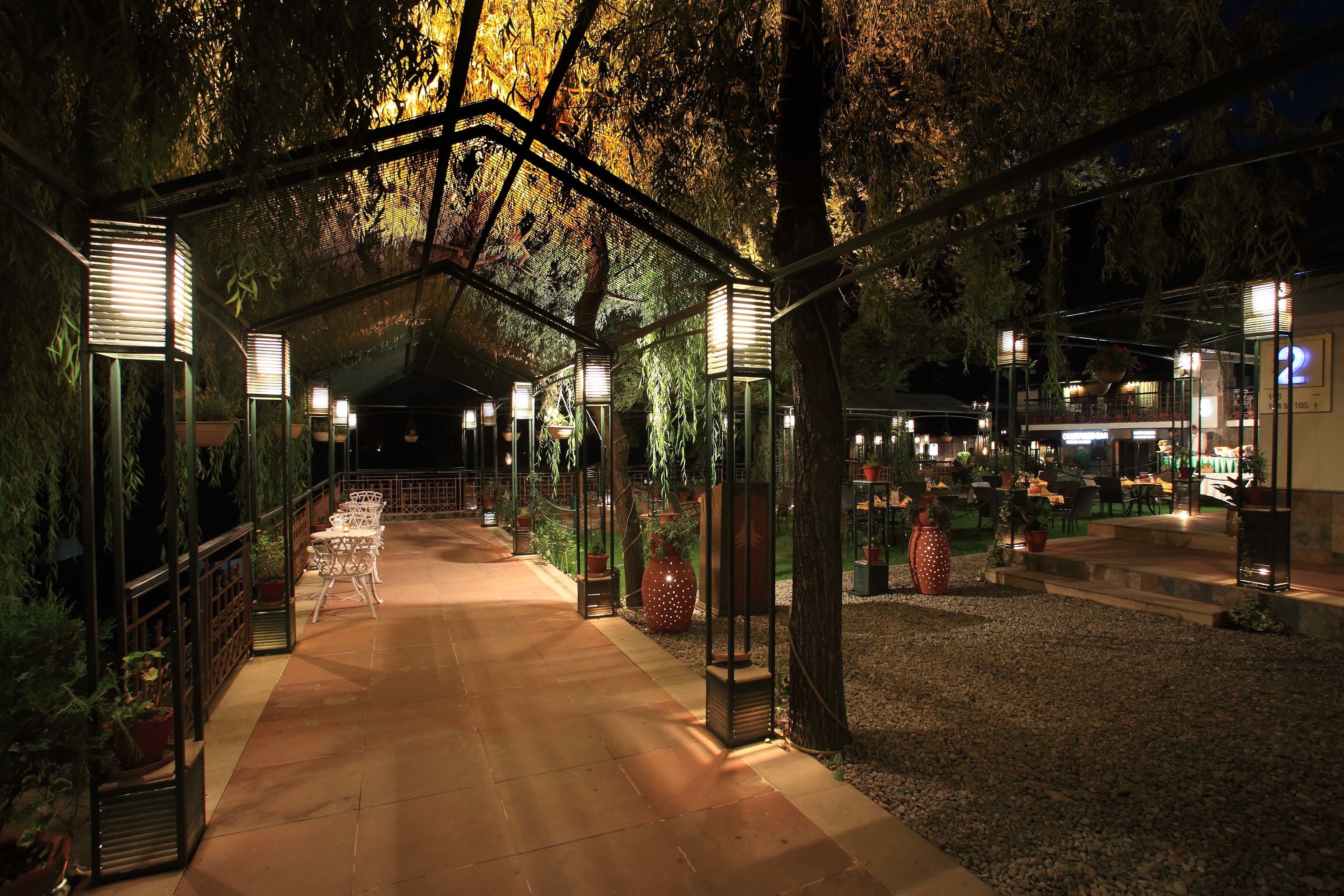 A covered pathway with potted plants and outdoor seating, leading to a building with a sign that reads "2".