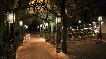 A covered pathway with potted plants and outdoor seating, leading to a building with a sign that reads "2".