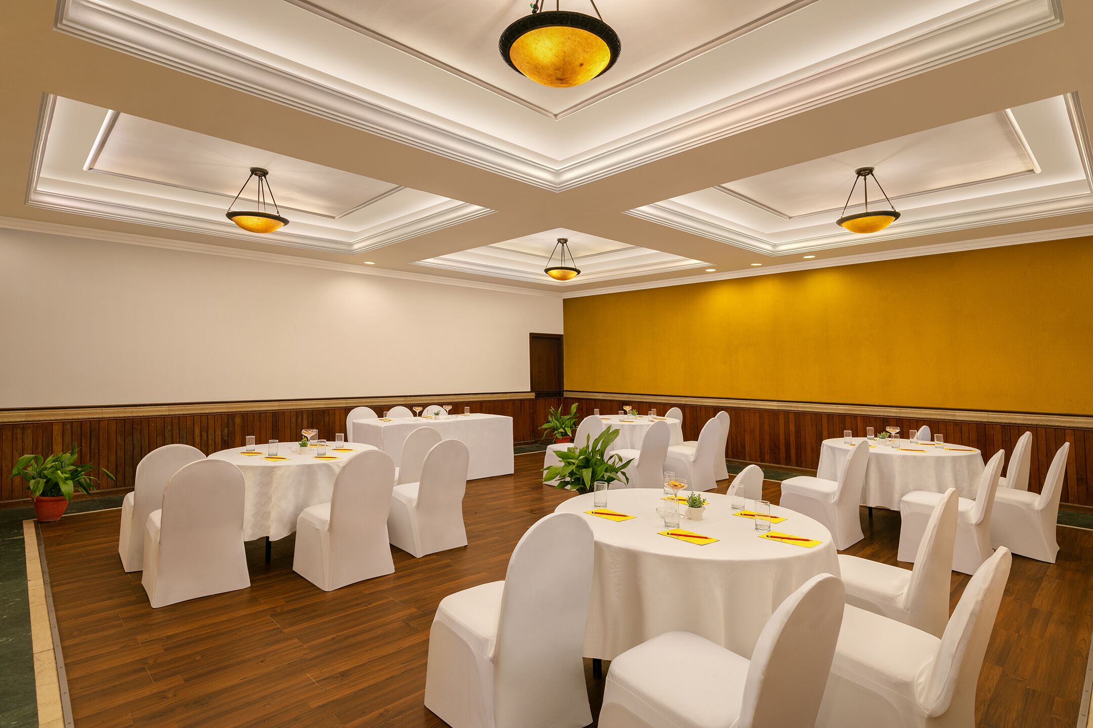 A conference room with round tables, white chairs, and chandeliers.
