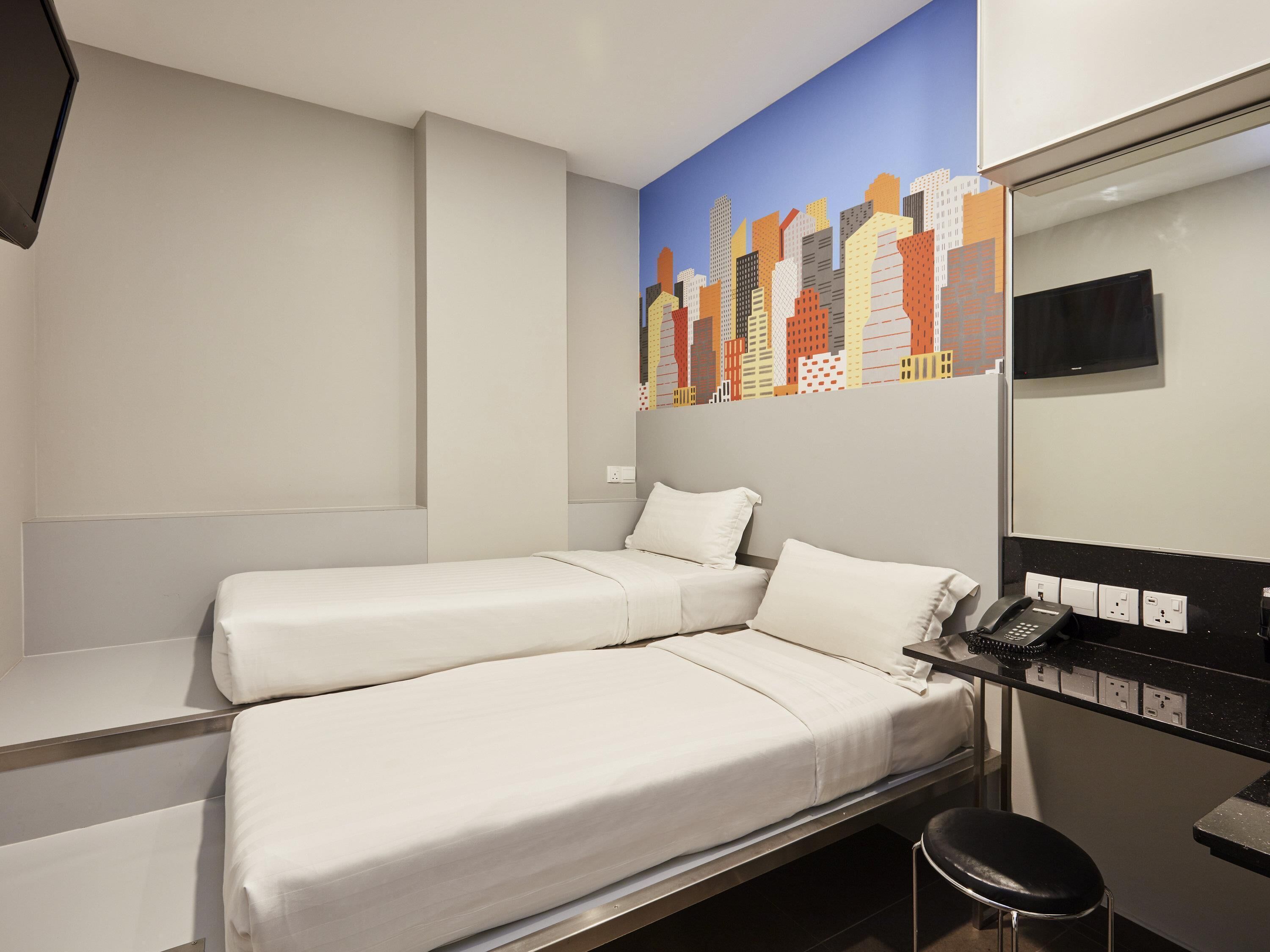 A hotel room with two beds, a desk with a telephone, and a cityscape mural on the wall.