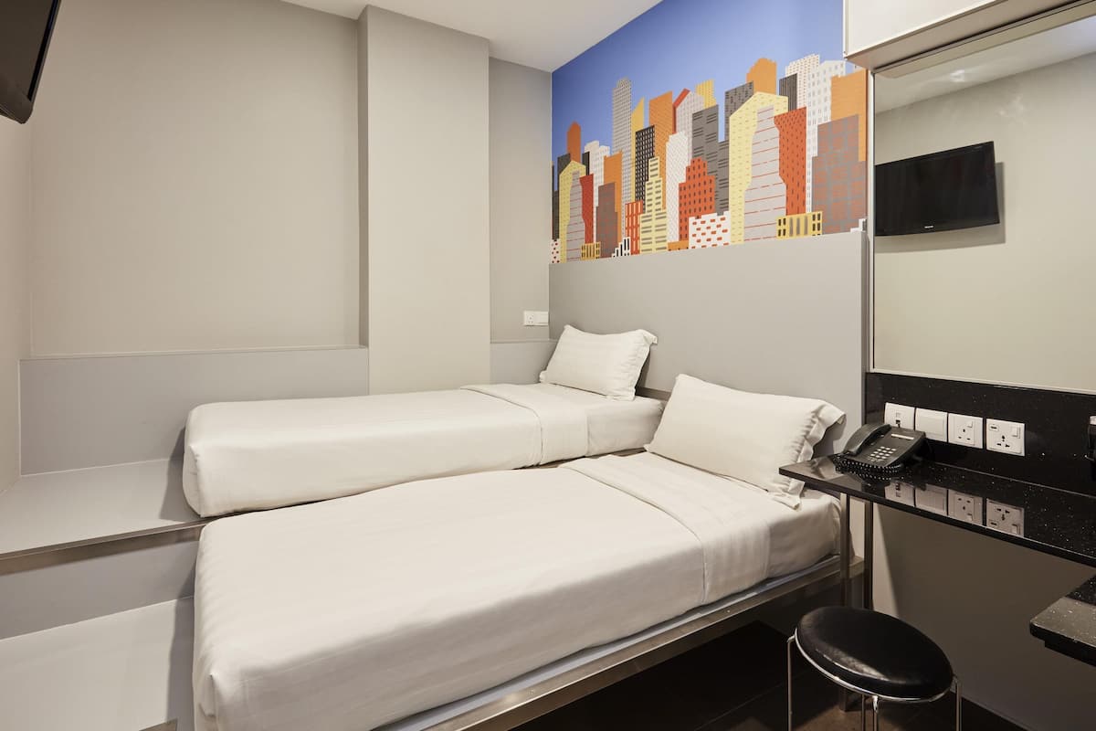 Quarto de hotel com duas camas, uma escrivaninha com telefone e um mural com vista para a cidade.
