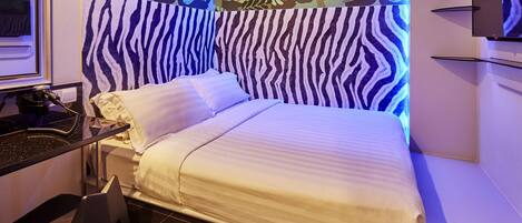 A modern hotel room with a zebra-striped headboard, a bed with white linens, and a wall with a leaf pattern.