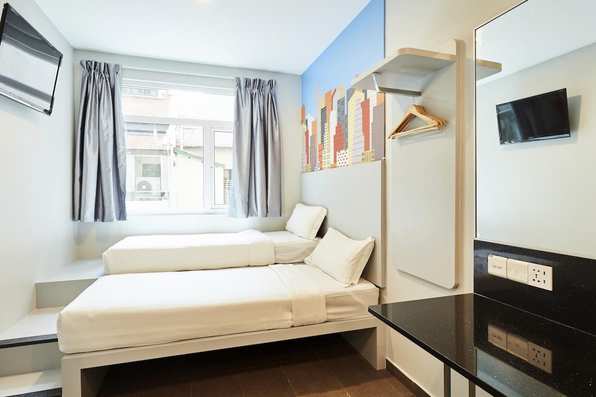 A hotel room with a bed, a desk, a TV, and a window with curtains.