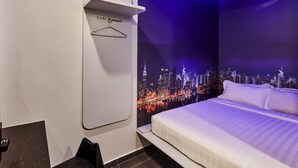Una habitación de hotel con una cama, un perchero en la pared y un mural con vista a la ciudad.