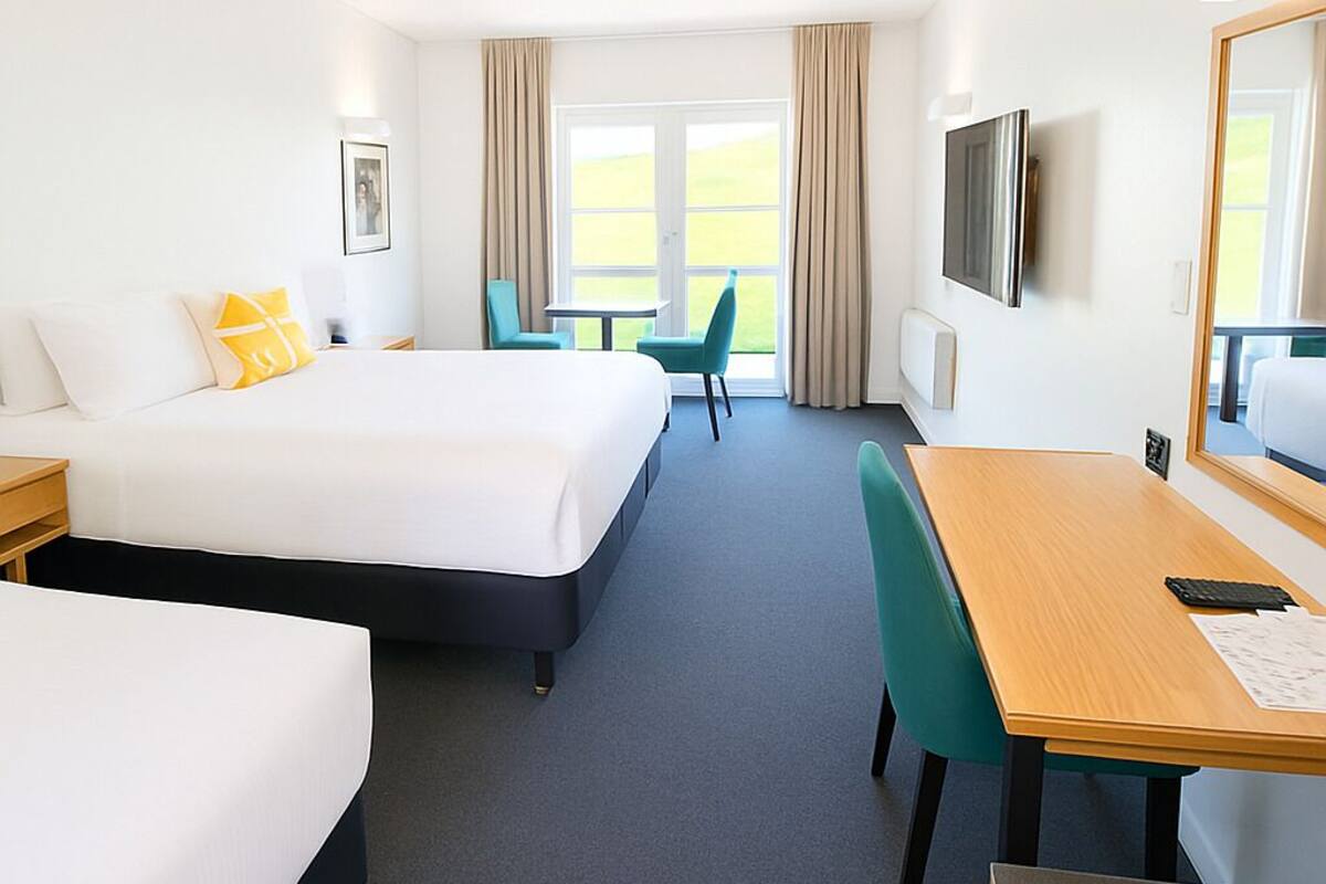 A hotel room with a large bed, a desk, a chair, a TV, and a window with curtains.