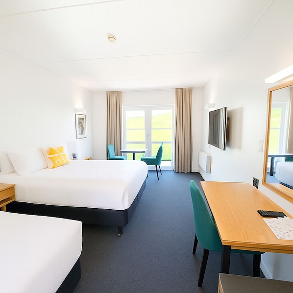 A hotel room with a large bed, a desk, a chair, a TV, and a window with curtains.