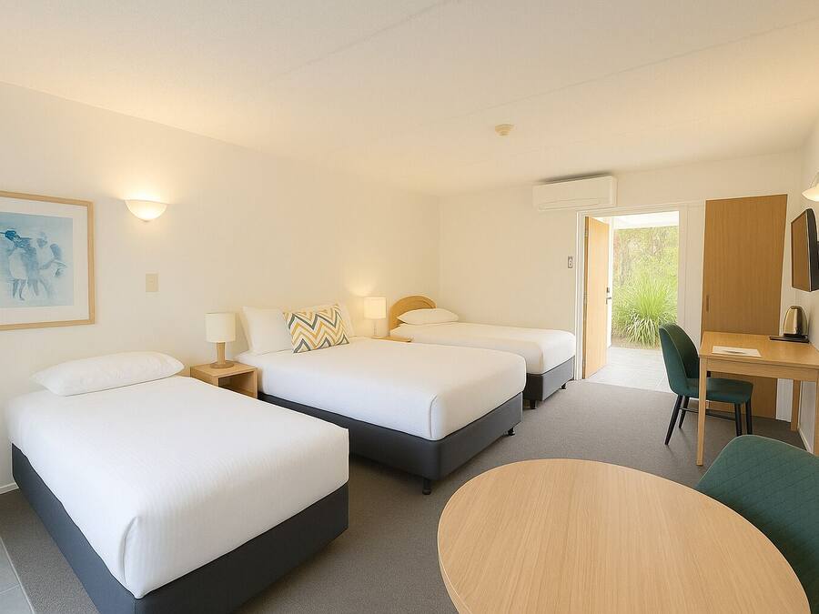 Een hotelkamer met twee bedden, een bureau, een stoel en een ronde tafel.