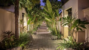 A paved pathway flanked by lush tropical plants and palm trees, leading to a building entrance. - The Tukad Villa (Seminyak)