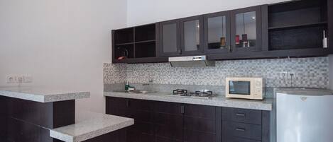 A kitchen with dark cabinets, a microwave, a stove, and a refrigerator.