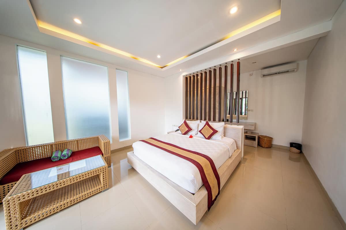 A modern hotel room with a large bed, a wicker sofa, and a glass table.