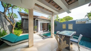 A modern outdoor pool area with a glass table and lounge chairs, surrounded by a blue wall and a wooden pergola. - The Tukad Villa (Seminyak)