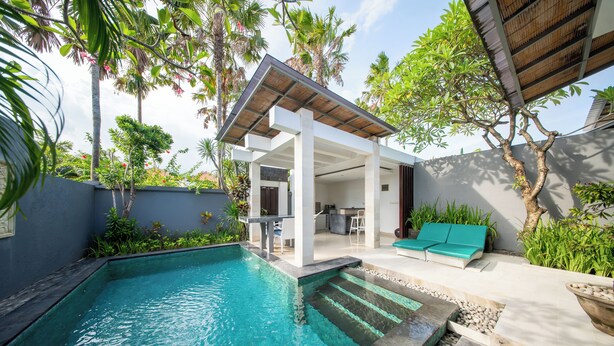 A swimming pool with steps leading into it, surrounded by a covered patio area with seating and a kitchen visible in the background. - The Tukad Villa (Seminyak)