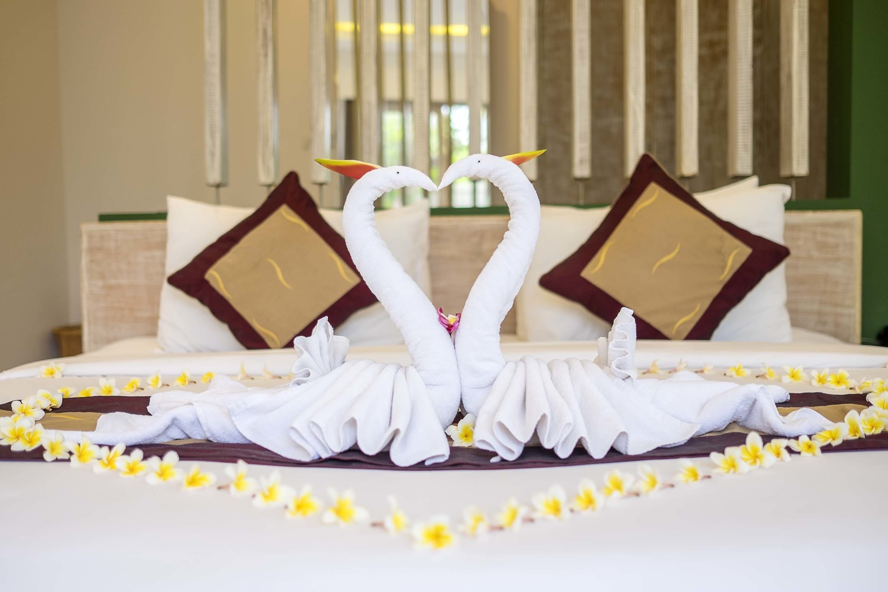 A hotel room with a bed adorned with towels shaped like swans and yellow flowers.