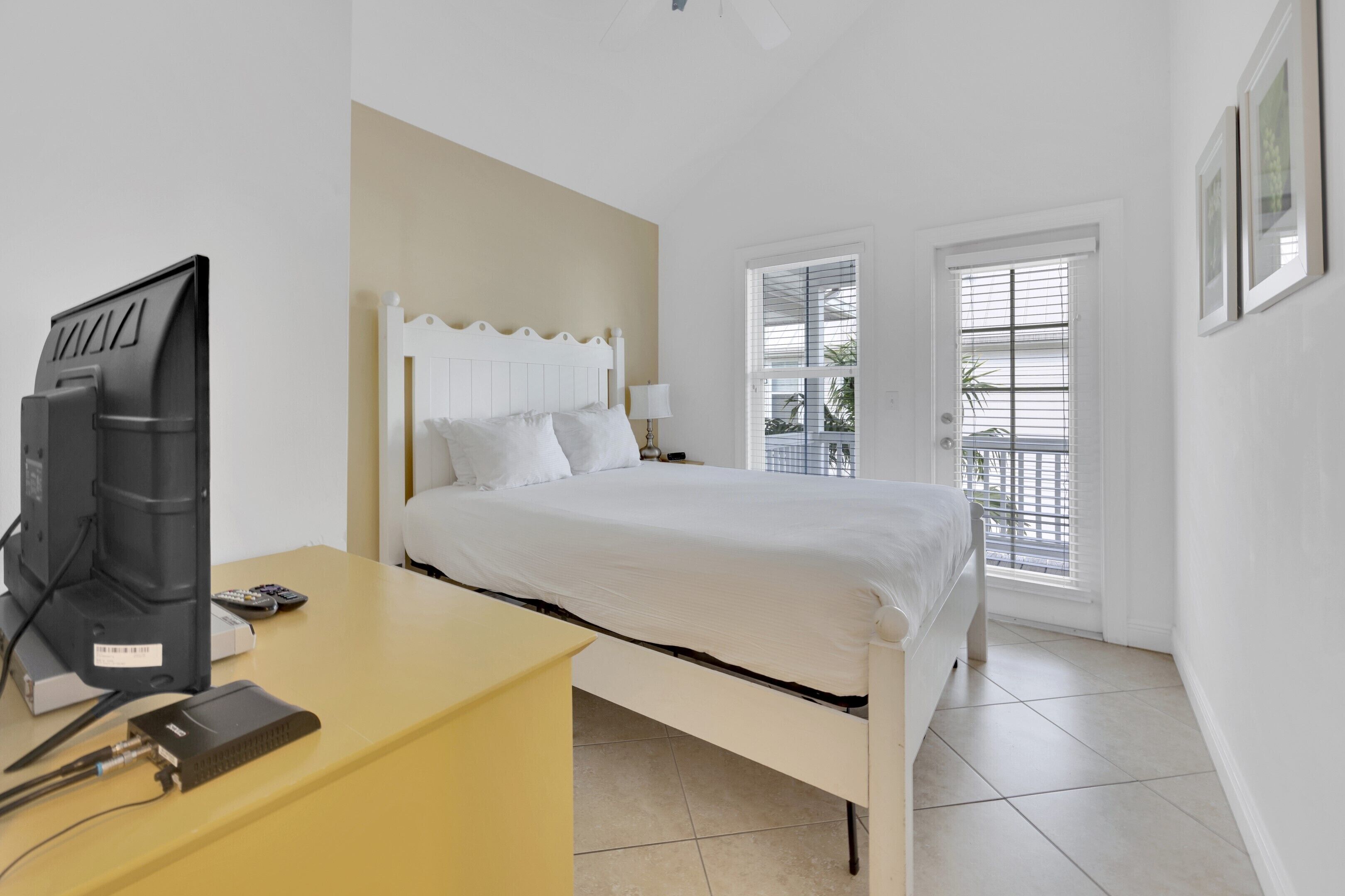 Un dormitorio con una cama, un escritorio con computadora y un televisor.