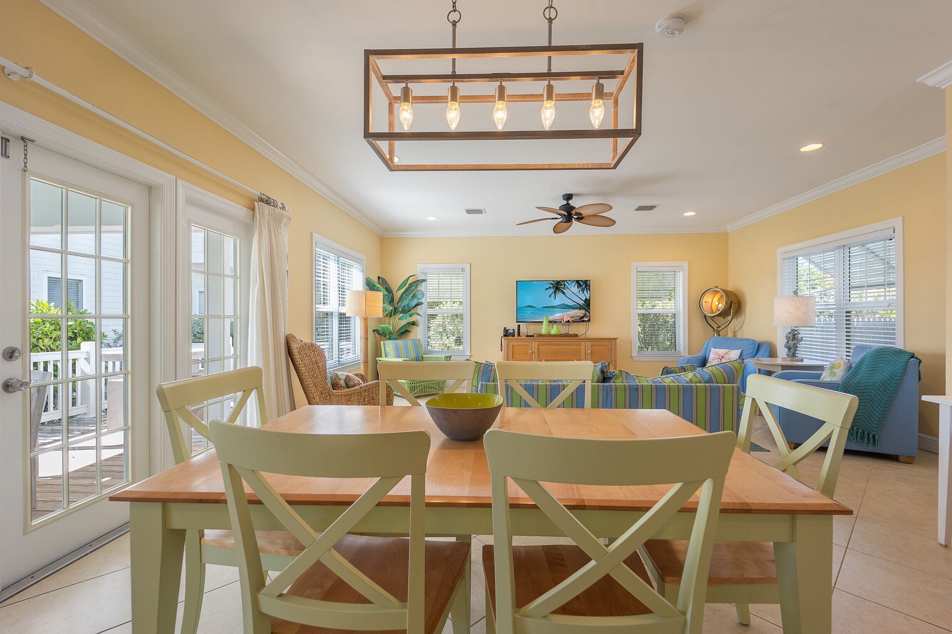 A dining area with a wooden table and chairs, a ceiling fan, and a view of the outdoors.