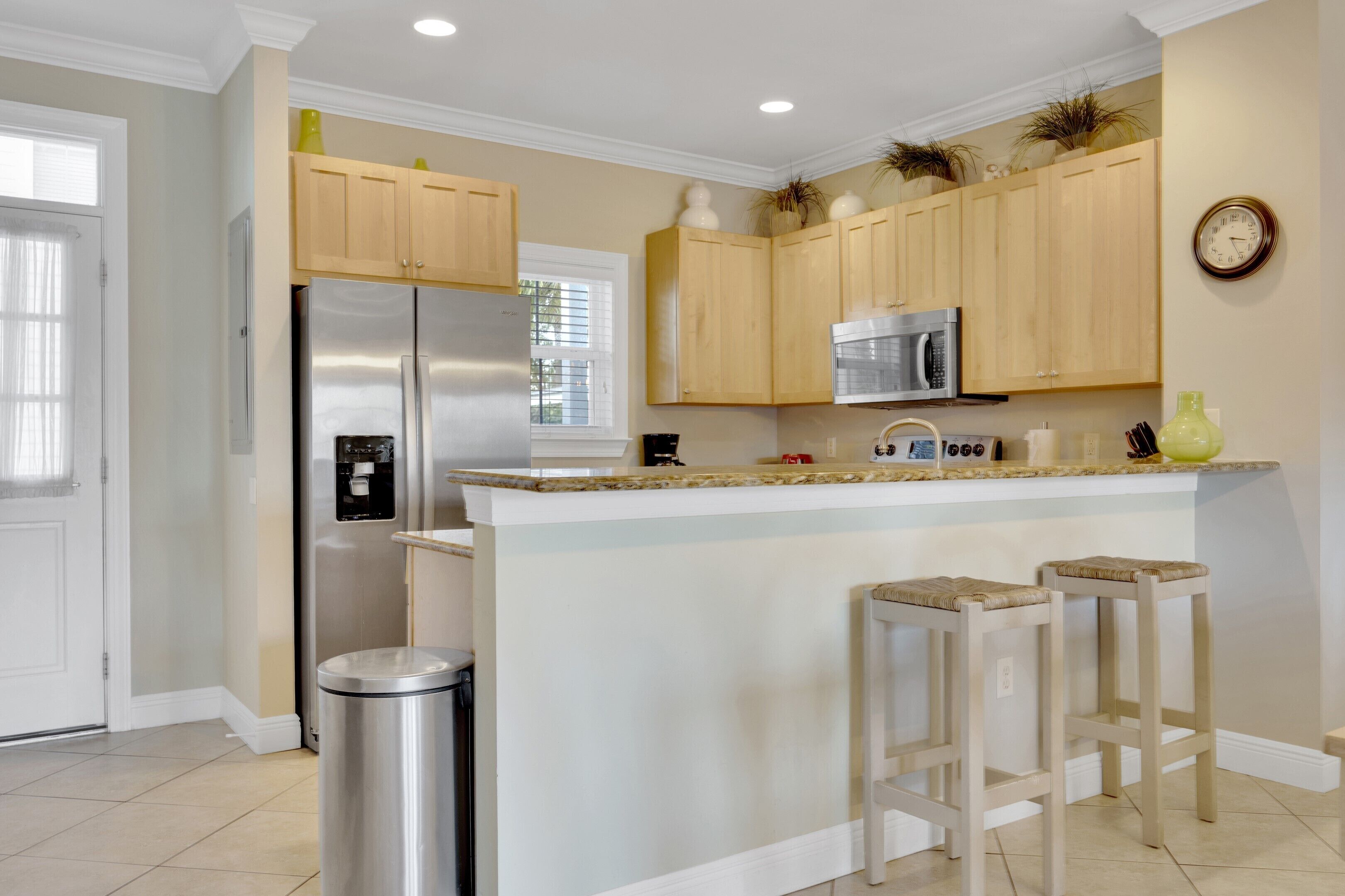 Une cuisine moderne avec des meubles en bois, des appareils en acier inoxydable, un îlot central doté de tabourets et une horloge au mur.