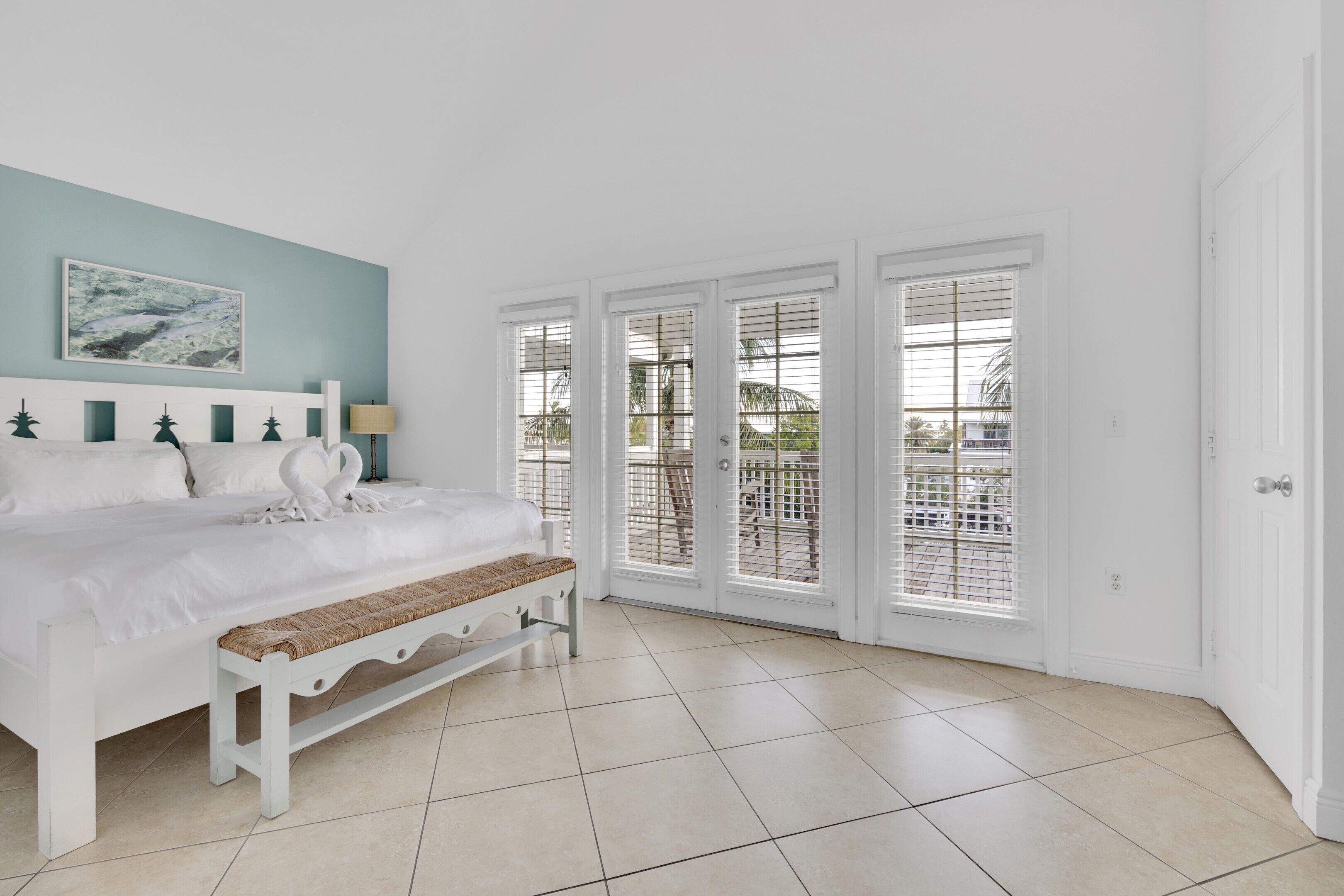 Une chambre à coucher avec un lit, un banc et de grandes fenêtres équipées de stores.