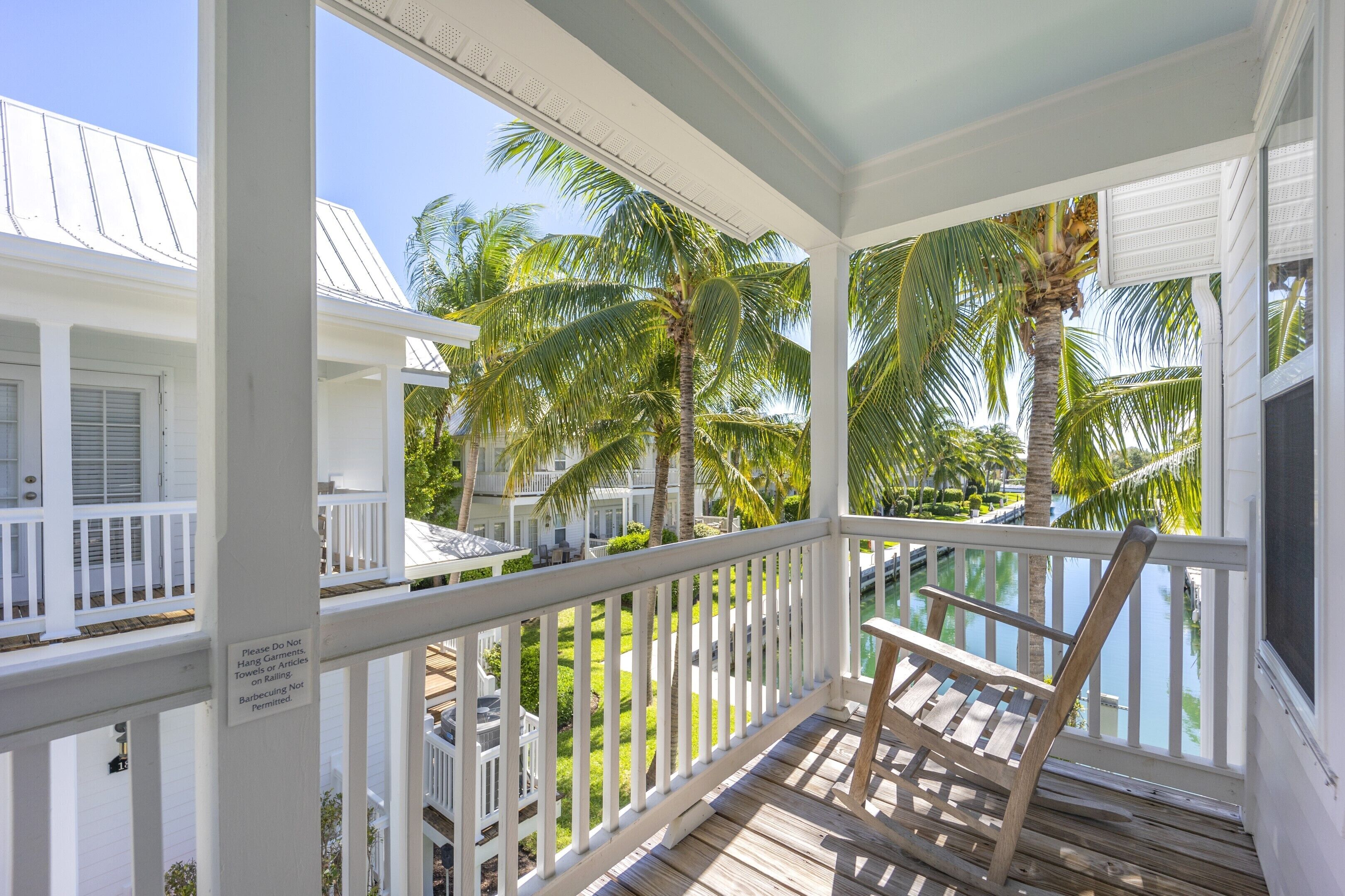 A wooden deck with a white railing, overlooking a pool and palm trees.