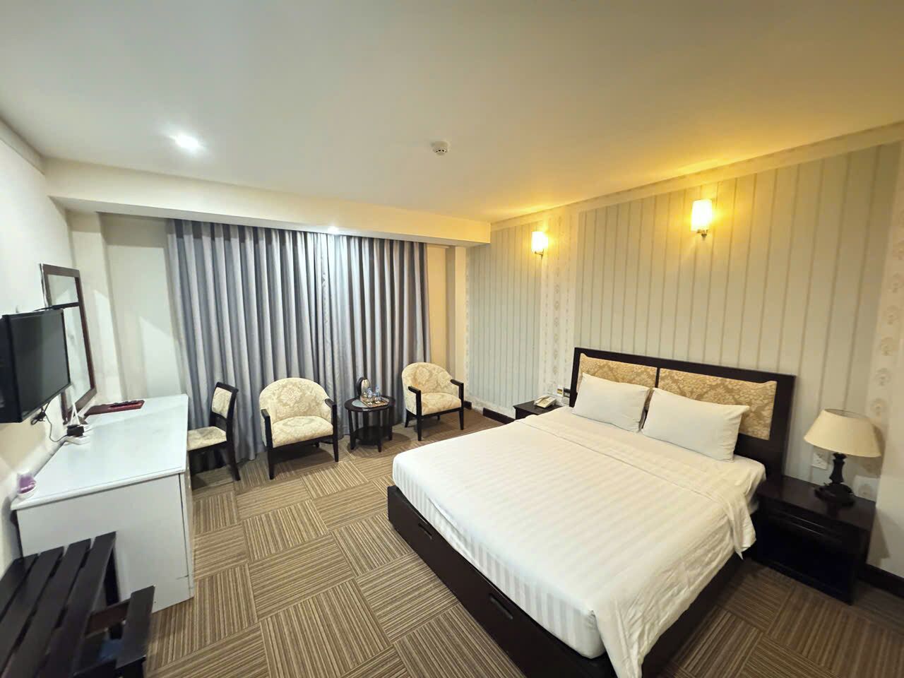 Habitación de hotel con cama, dos sillones, escritorio con televisor y mesita de noche con lámpara.