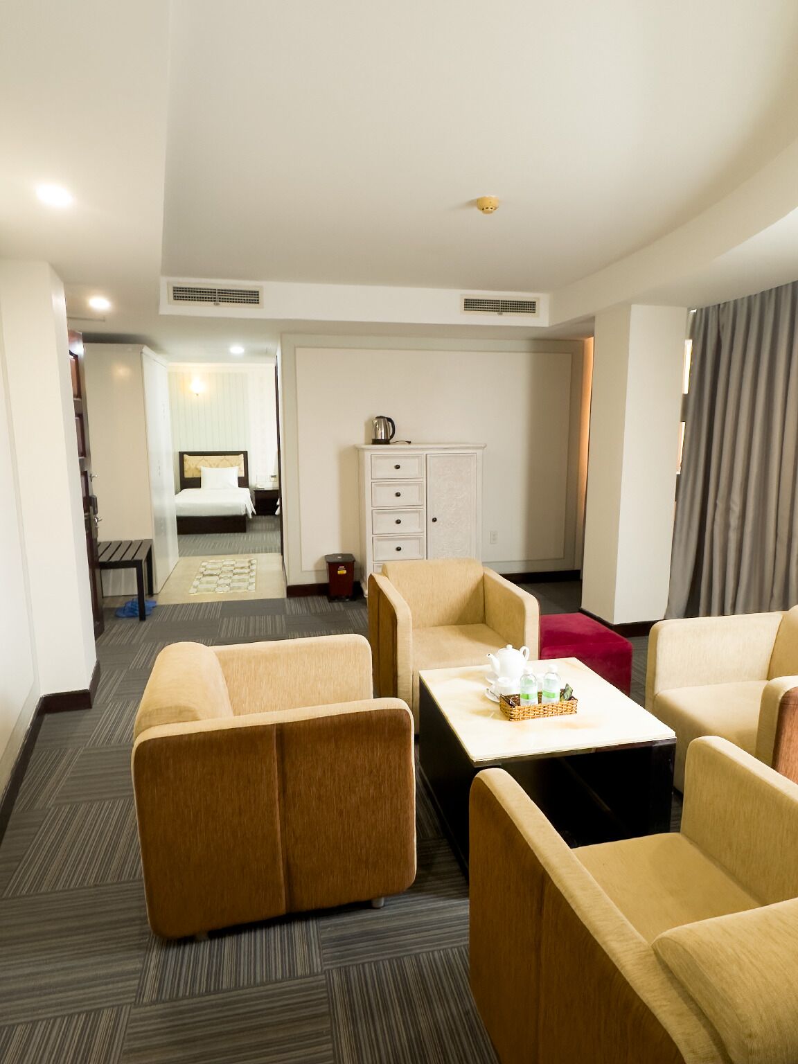 Ein Hotelzimmer mit einem Bett, einem Schreibtisch, zwei Sesseln, einem kleinen Schrank und einem roten Hocker.