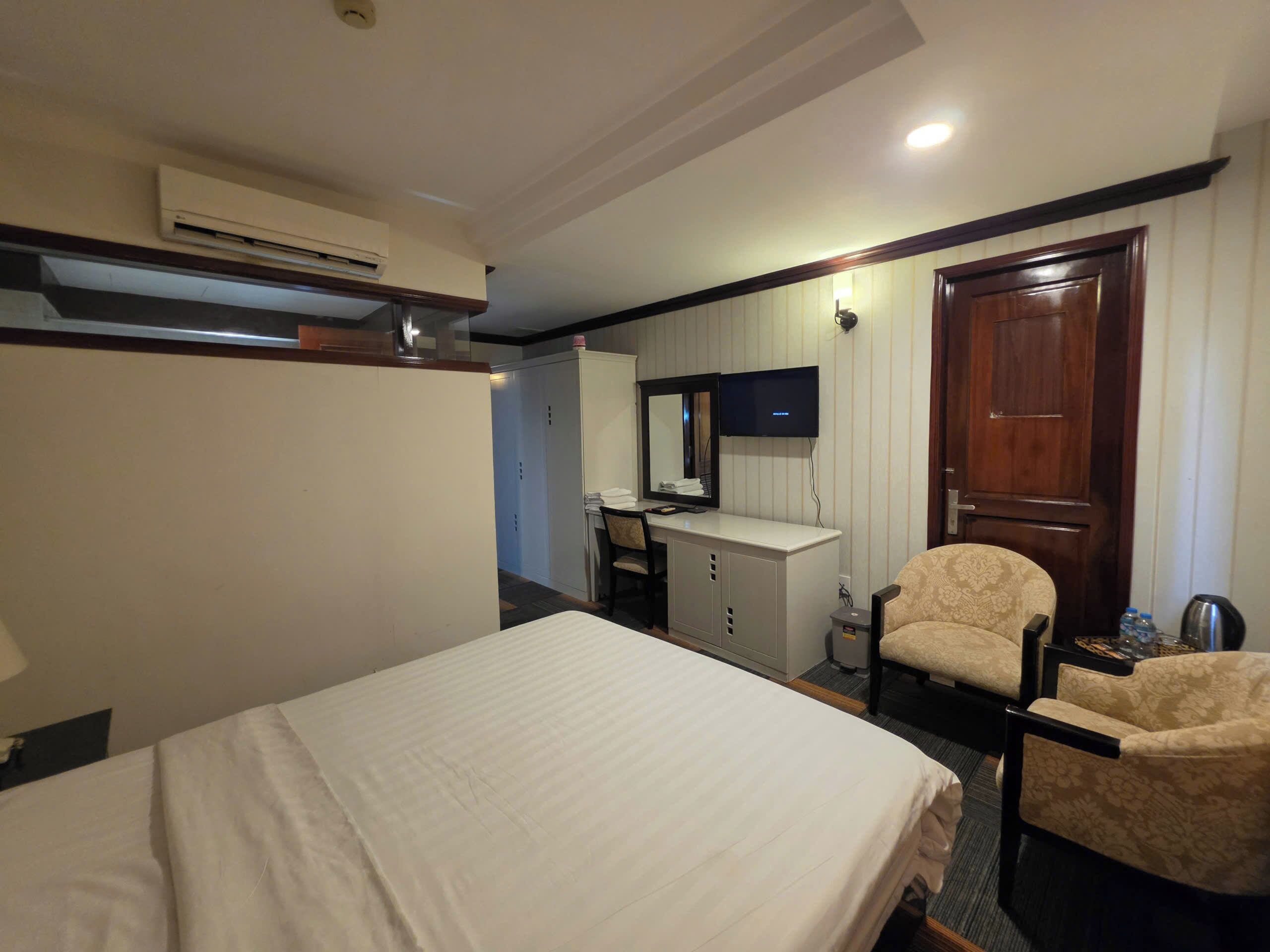 A hotel room with a bed, a desk with a chair, a television, and a wardrobe.