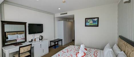 A hotel room with a bed, a desk, a chair, a television, a wardrobe, and a painting on the wall.