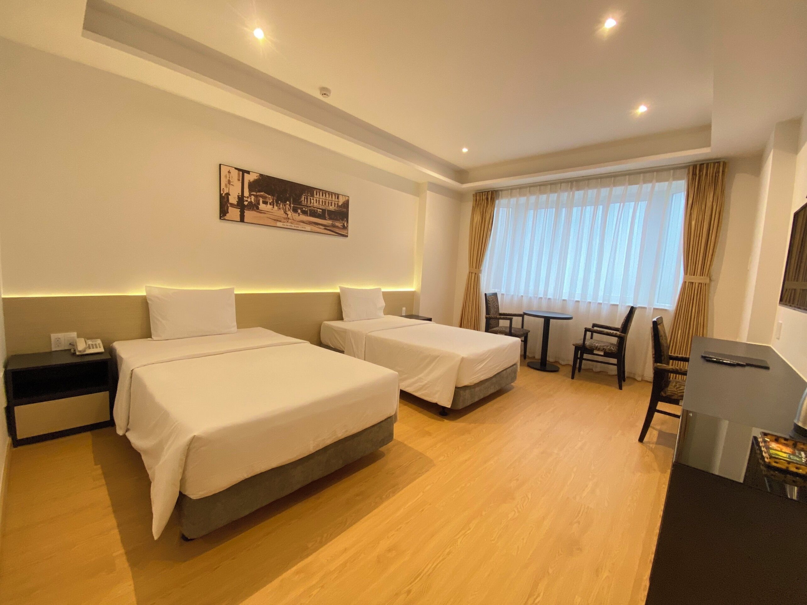 A hotel room with two beds, a desk, a chair, and a table.