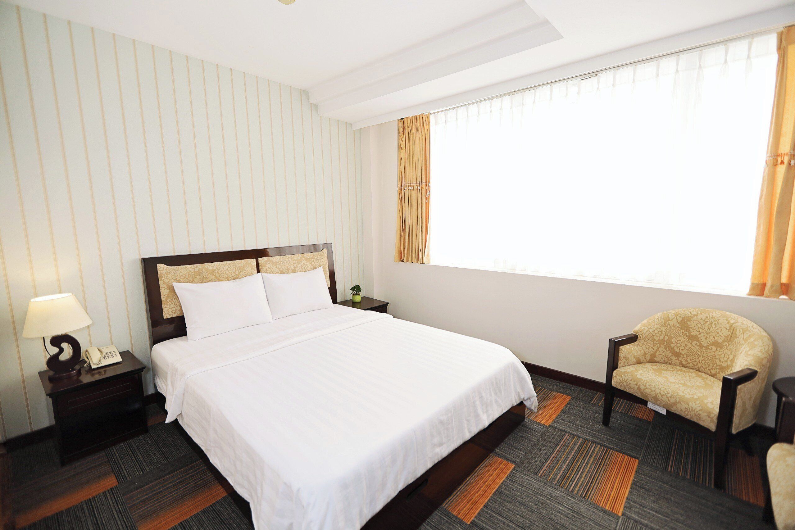 Ein Hotelzimmer mit einem großen Bett, einem Sessel, einem Nachttisch mit Lampe und einem Fenster mit Vorhängen.